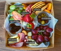 an open box filled with different types of cheeses, fruit and crackers on top of a wooden table