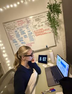 a woman sitting in front of a laptop computer on top of a wooden desk next to a plant