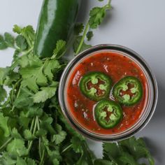 three hot sauces in a bowl with green peppers and cilantro on the side