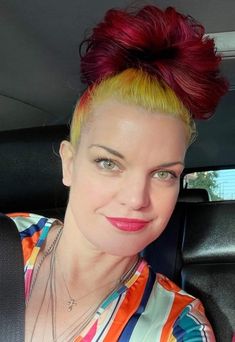 a woman with red and yellow hair sitting in the back seat of a car looking at the camera