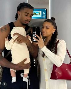 a man and woman holding a baby in their arms while looking at a cell phone