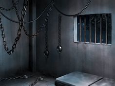 a jail cell with bars and chains hanging from the ceiling, next to a bench