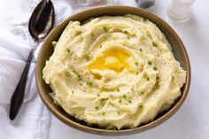 a bowl filled with mashed potatoes on top of a white cloth next to a spoon