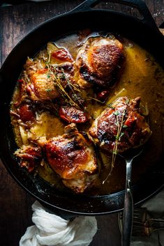 some meat in a skillet on a table next to a spoon and napkins