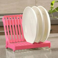 three plates are stacked up on a pink dish rack next to a potted plant