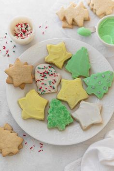 decorated cookies on a white plate next to bowls of sprinkles and sugar