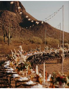 a long table is set up in the desert for an outdoor dinner party with lights strung over it