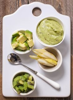 three small bowls filled with different types of food on a white tray next to two spoons