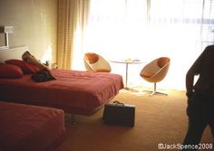 two beds in a hotel room with one person standing next to the bed and another chair