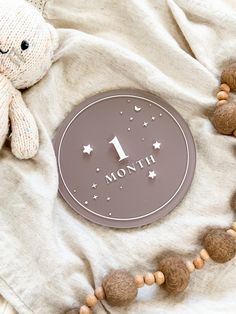 a wooden bead necklace with a one month sign on it next to a teddy bear