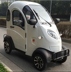 the small car is parked on the side of the road in front of some bushes