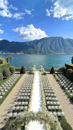 an outdoor ceremony set up with rows of chairs in front of the water and mountains