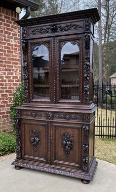 an old wooden china cabinet sitting on top of a cement floor next to a brick building