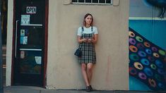 a woman leaning against a wall with her hand on her hip looking at the camera