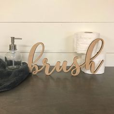 a wooden brush sign sitting on top of a table next to a toilet paper dispenser