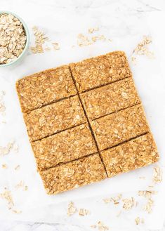 oatmeal bars cut into squares on top of a white surface next to a bowl of oats