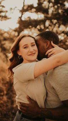 a man and woman embracing each other in front of some trees with the sun shining on them