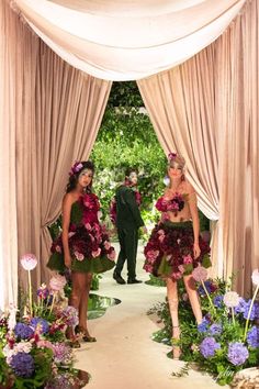 two women dressed in green and pink dresses are walking down the aisle with flowers all around them