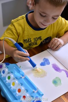 a little boy that is sitting at a table with some watercolors on it