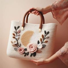 a woman holding a white bag with flowers on it and a brown handle in her hand