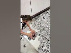 a woman is washing dishes in a kitchen with lots of silver foil on the floor