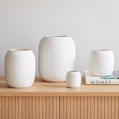 three white ceramic vases sitting on top of a wooden table next to a book