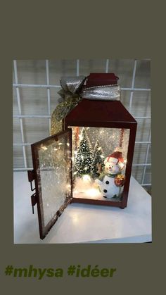 a lighted lantern with a snowman and christmas tree in the front, sitting on a table