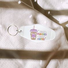 a keychain with a coffee drink on it sitting on top of a white sheet