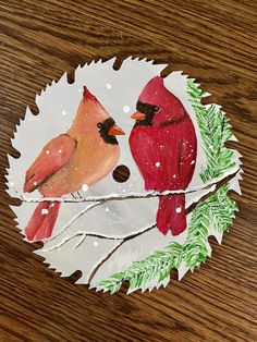 two red birds sitting on top of a white paper plate covered in pine cones and branches