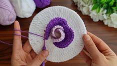 two hands are holding a crocheted object with yarn on the table next to flowers