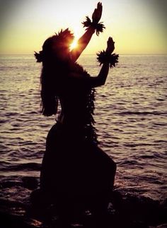 a woman standing on top of a beach next to the ocean with her hands in the air