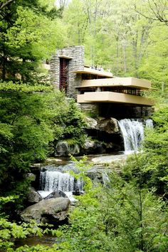 a house in the woods surrounded by trees and rocks with water running down it's side