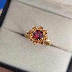 Embrace the beauty of nature with this enchanting golden sunflower ring. The centerpiece of this captivating piece is a round red garnet, radiating warmth and passion. It is encircled by a halo of citrine rounds, each one shimmering with an irresistible glow, reminiscent of the sun's golden rays. The combination of the vibrant red garnet and the sparkling citrine creates a harmonious contrast, symbolizing the essence of a blooming sunflower. Crafted in silver, the ring adds a touch of elegance a Citrine And Garnet Ring, Garnet Birthstone Cluster Ring, Anniversary Rings With Sunflower Design, Blooming Sunflower, Golden Sunflower, Design Your Own Ring, Sunflower Ring, Golden Flower, Citrine Ring