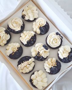 twelve cupcakes with white frosting and black icing in a cardboard box