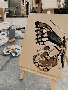 a woman standing next to an easel with a butterfly painted on it's side