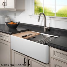 a white kitchen sink sitting under a window next to a bowl of fruit on top of a counter