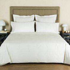 a bed with white sheets and pillows in a bedroom next to a night stand on the floor