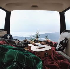 an open car window with blankets and guitar on the bed in it, overlooking mountains