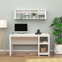 a white desk with a computer on it in front of a green plant and lamp