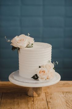 a wedding cake with white frosting and fresh flowers on the top is sitting on a wooden table