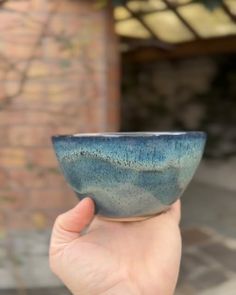 a hand holding a blue bowl in front of a brick building