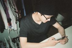 a young man sitting at a table looking at his cell phone while wearing a beanie