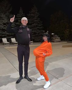 an older man and woman in orange outfits posing for a photo at night with trees in the background