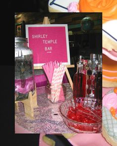 a table topped with lots of different types of desserts and drink glasses next to a sign