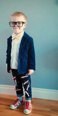 a young boy wearing glasses and a bow tie standing in front of a blue wall