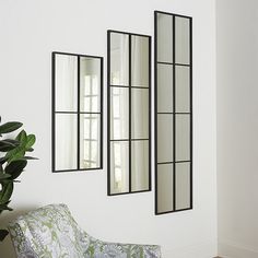 three mirrors are hanging on the wall near a chair and potted plant in front of it