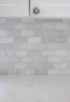 a kitchen counter top with white cabinets and marble tile backsplash in the background