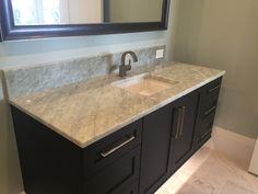 a bathroom vanity with marble counter top and black cabinetry, along with a large mirror over the sink