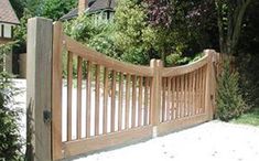 a large wooden fence in front of a house with trees and bushes around it,