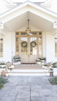 the front door of a white house with wreaths and lanterns on it's steps